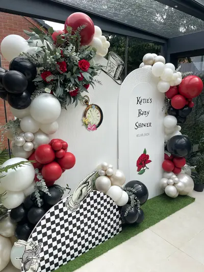 Baby shower decor in Stoney Stanton by Lulu Belle Events. Alice in Wonderland. Red, black, white and silver/cream. Full organic balloon garland wrapping around both sides and top of the arched backdrop. Red, black, white, cream and silver/chrome.
