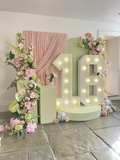 Birthday decor in Groby by Lulu Belle Events. Blush pink, sage green, white and silver. Floral birthday with retro arch and disco ball accents. Multiple small silver mirror disco balls scattered at the base of the display on both sides.