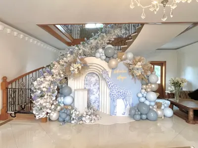 Baby shower decor in Upper Bruntingthorpe by Lulu Belle Events. White hydrangeas, white and cream roses or similar blooms, blue/lavender florals, dried pampas grass, and dried palm fans. Safari / giraffe. Dusty blue, sage grey, cream, champagne/gold, white, with touches of lavender in the florals.