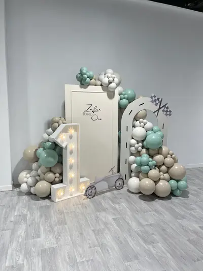 First birthday decor in Leicester by Lulu Belle Events. Racing / motor car. Sage green, sand/beige, white, grey. Organic balloon garland in sage green, sand/beige, white and grey, running across the top of the backdrop and down both sides, extending to ground level on each side. Sage green, sand/beige, white, grey.