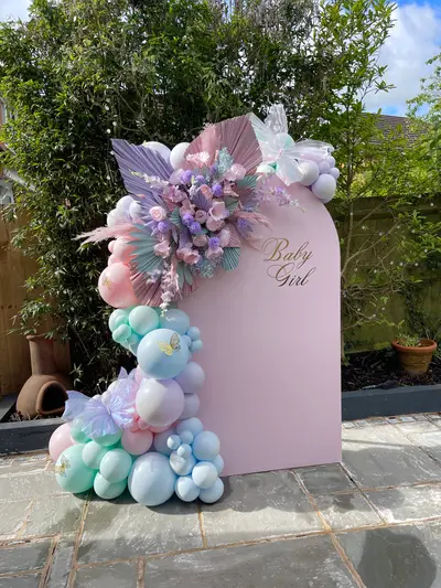 Baby shower decor in Ibstock by Lulu Belle Events. Butterfly and floral baby shower in pastel tones. Pastel pink, mint green, lilac, baby blue, and white with gold accents. Outdoor residential garden. Arch-top panel with rounded top, flat sides and base.