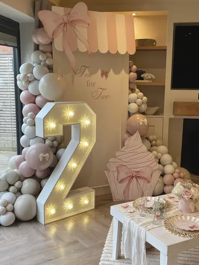 Birthday decor in Sheepy by Lulu Belle Events. Tea for Two. Full balloon garland wrapping around both sides of the backdrop, extending from floor to above the backdrop. Blush pink, warm white, cream/nude, and greige/taupe in mixed sizes. Organic-style garland with varying balloon sizes, no foliage.