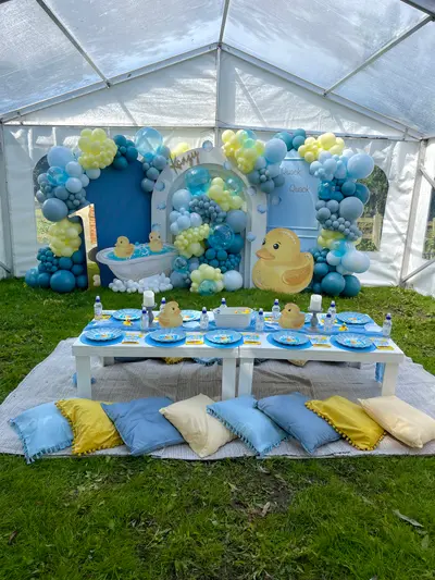 Birthday decor in Leicester by Lulu Belle Events. Clear-sided marquee on grass. Rubber duck / bath-time. Baby blue, teal, yellow and white. White centrepiece bowl/vessel placed centrally on the table.