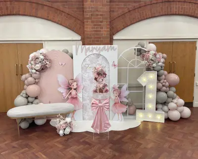First birthday decor in Leicester by Lulu Belle Events. Fairy / Fairy First. Dusty pink, mauve, grey, white, and gold. Organic balloon garland framing the left and right sides of the backdrop display. Dusty pink, mauve, grey/sage, white, and nude/blush tones.