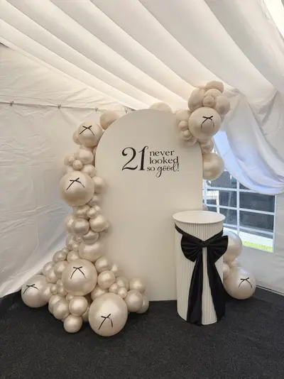 Birthday decor in Broughton Astley by Lulu Belle Events. Marquee interior. Cream, ivory and black. Arch-top panel (rounded top, flat base). Organic balloon garland framing the arch backdrop, concentrated heavily on the left side and looping over the top.