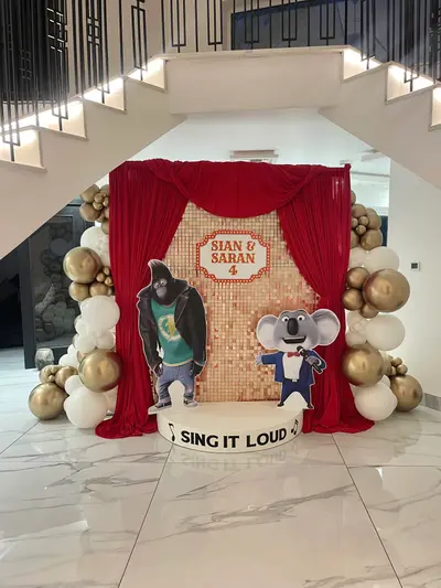 Birthday decor in Oadby by Lulu Belle Events. Sing (animated film). Red, gold, and white. Organic balloon garland arch framing both sides of the backdrop. Chrome gold, white, and matte white/cream in varying sizes.