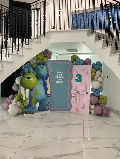 Birthday decor in Oadby by Lulu Belle Events. Monsters Inc. Organic balloon garland draping across the top and sides of the backdrop and around the character cutout. Mauve/dusty purple, olive green, teal/blue, white and cream. Organic cluster style with mixed balloon sizes.