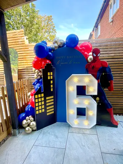 Birthday decor in Leicester by Lulu Belle Events. Organic balloon garland draped across the top and left side of the arch backdrop. Royal blue, red, chrome gold. Royal blue, red, chrome gold, white. Spider-Man.