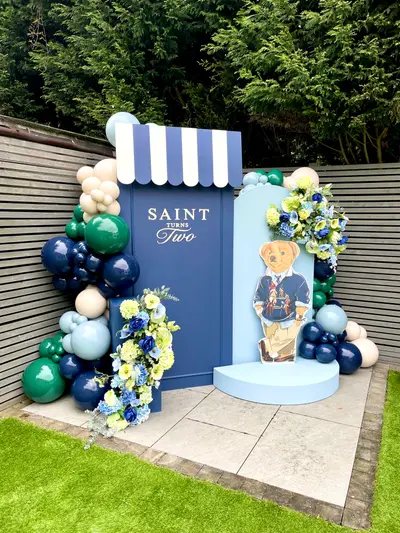 Birthday decor in Ravenstone by Lulu Belle Events. Polo Bear / preppy teddy bear. Navy blue, forest green, light blue, cream/nude, yellow and white. Organic balloon garland wrapping around both sides and across the top of the backdrop structure. Navy blue, forest green, sage/light blue, cream/nude.