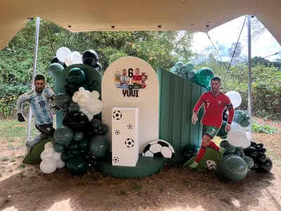 Event styling & planning in Swithland by Lulu Belle Events. Organic balloon garland displayed across the full width of the backdrop, concentrated on the left side and continuing around the right. Organic clustered arrangement with mixed balloon sizes. Dark forest green, sage/mid green, white, and black. Dark green, sage green, white, and black.